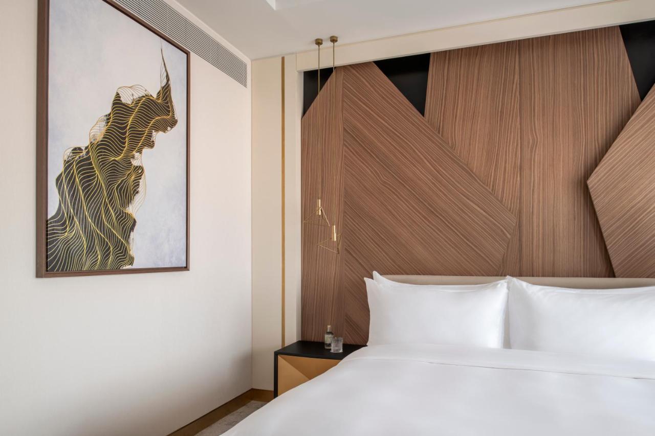 Steigenberger Hotel Doha Exterior foto The photo shows a modern hotel room with a clean and stylish design. The focal point is a large bed with white linens, set against a wall that features contemporary wooden paneling with geometric shapes. On the left side, there is a piece of artwork 