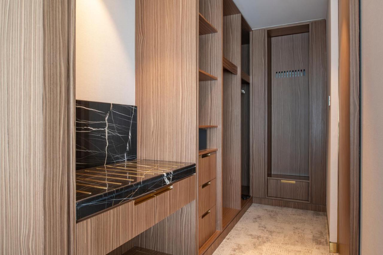 Steigenberger Hotel Doha Exterior foto The photo shows a well-designed interior space, likely a closet or dressing area. It features wooden cabinetry with a modern finish, including several open shelves for storage. There's a section with a dark marble countertop, which adds an elegant to