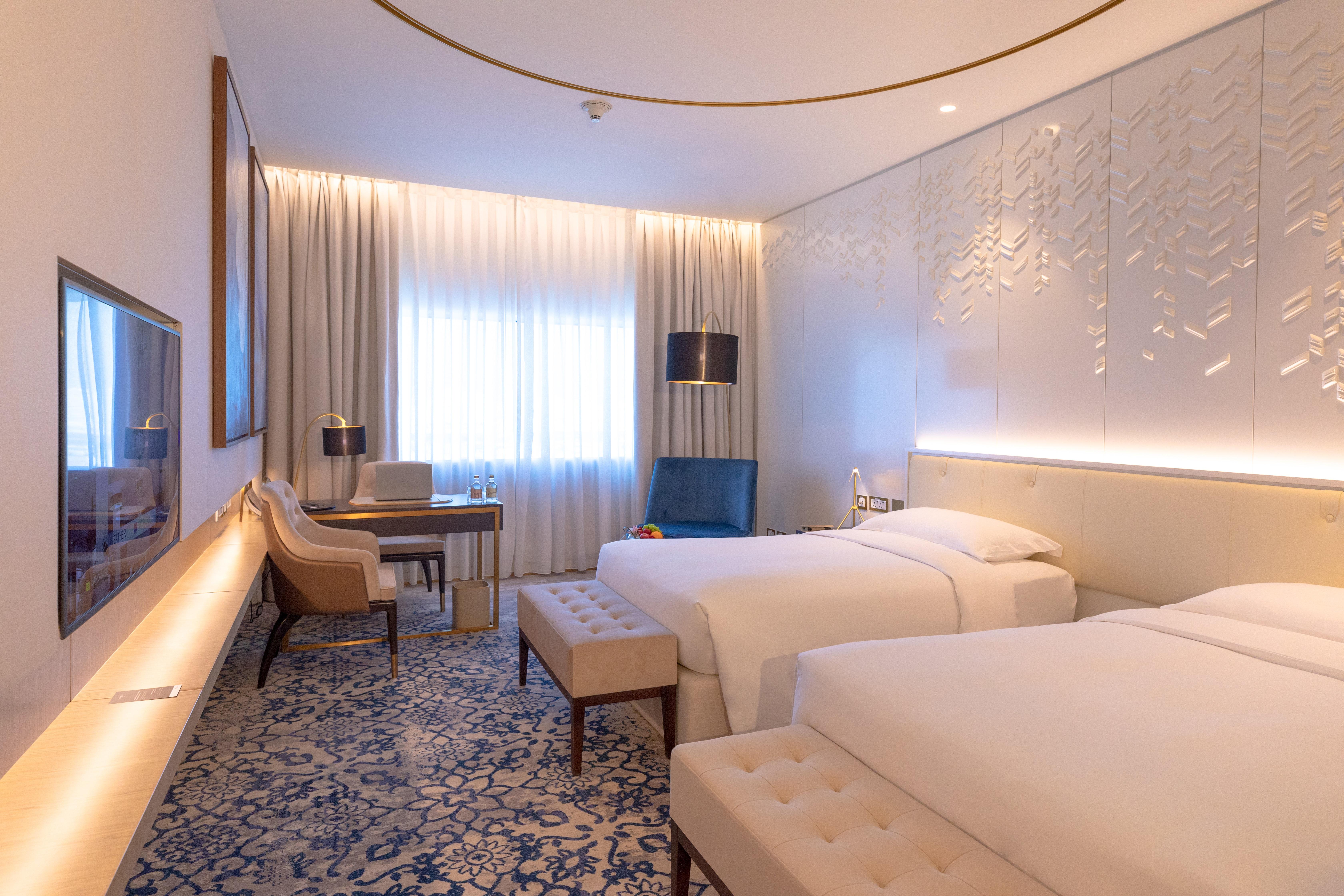 Steigenberger Hotel Doha Exterior foto The photo shows a modern hotel room with two single beds placed beside each other. The room features a contemporary design with light-colored walls and stylish decor. There is a large window dressed with sheer curtains, allowing natural light to fill