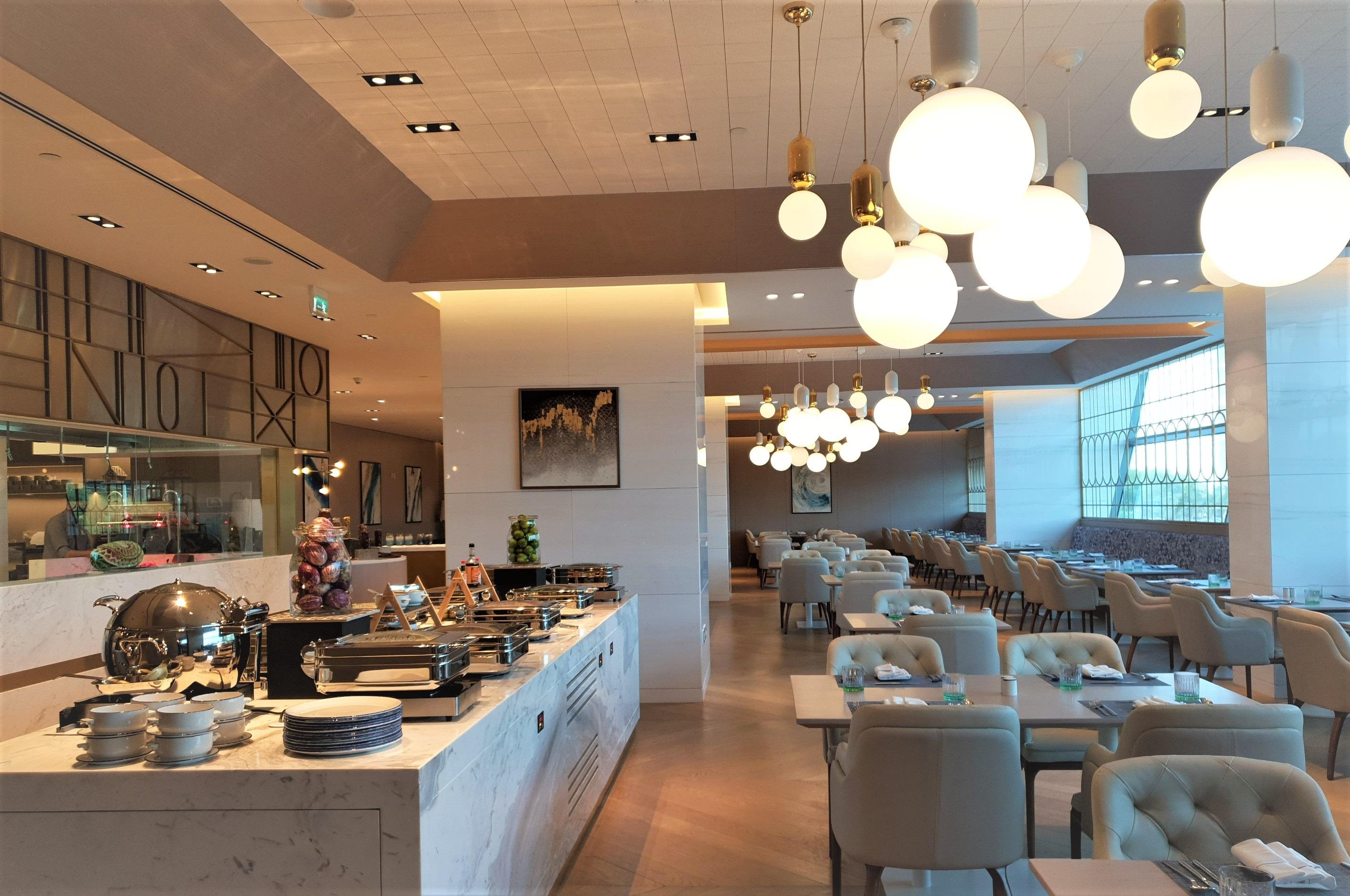 Steigenberger Hotel Doha Exterior foto The photo shows the interior of a modern restaurant. It features a well-organized buffet area with various dishes displayed on a marble counter. Elegant dining tables and chairs are set up throughout the space, creating a comfortable atmosphere. The 