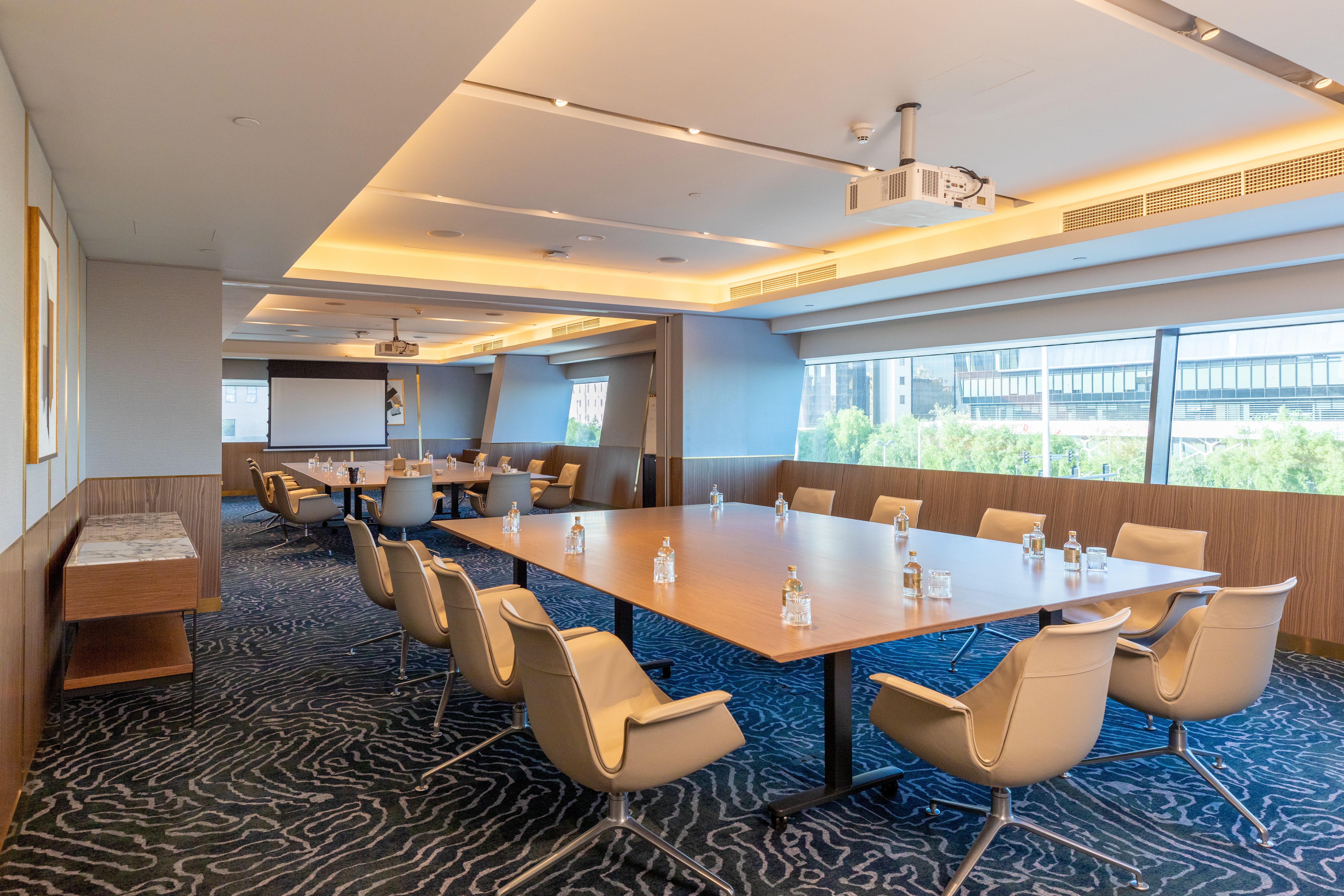 Steigenberger Hotel Doha Exterior foto The photo shows a modern conference room. It features large windows that let in natural light, illuminating the space. In the center, there is a large rectangular table surrounded by several ergonomic chairs. The table has glass water bottles on it, 