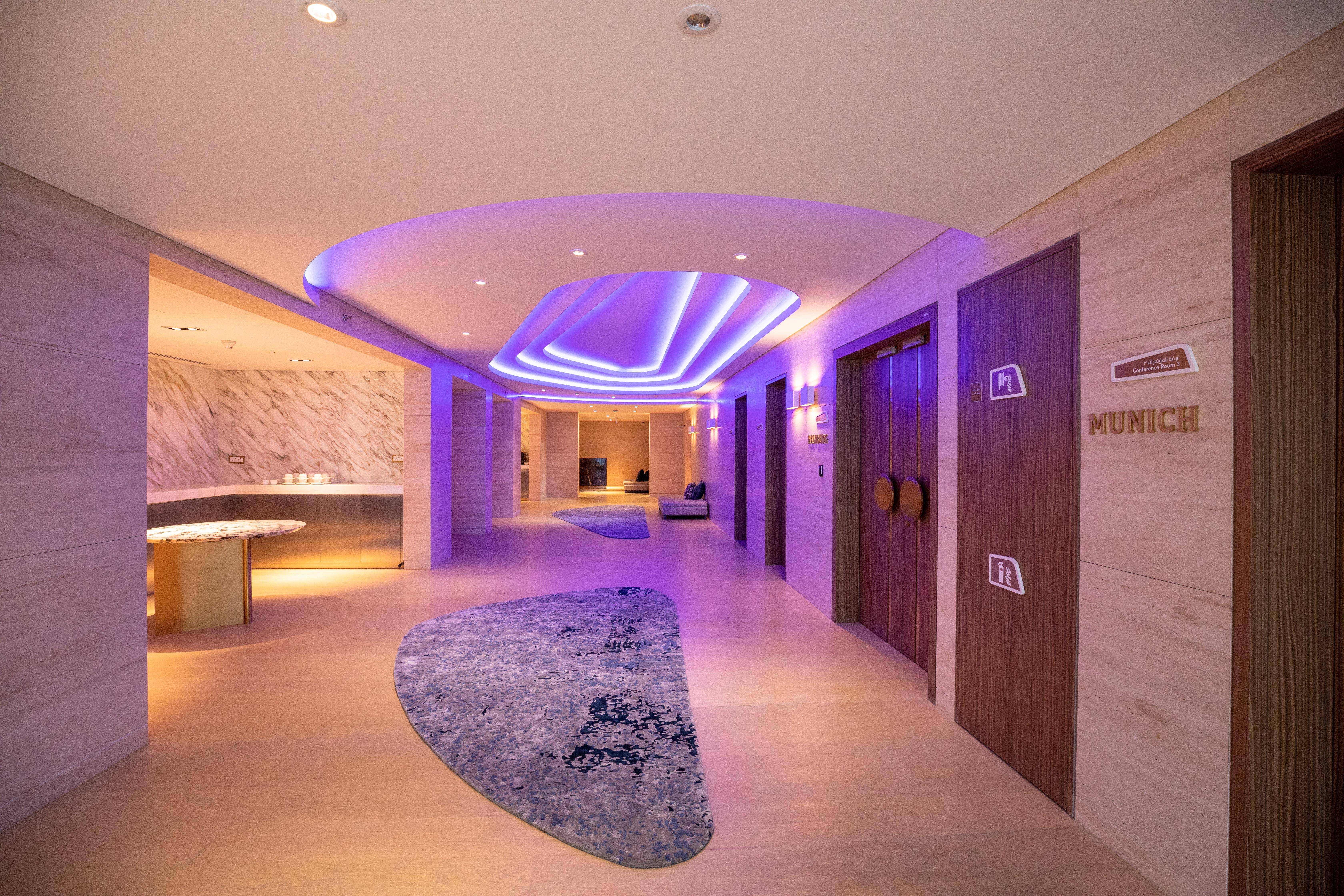 Steigenberger Hotel Doha Exterior foto The photo shows a modern hallway in a stylish setting. The corridor features soft, ambient lighting with a purple hue, creating a calming atmosphere. On the left side, there is a curved reception area with a smooth surface. The floor is decorated wit
