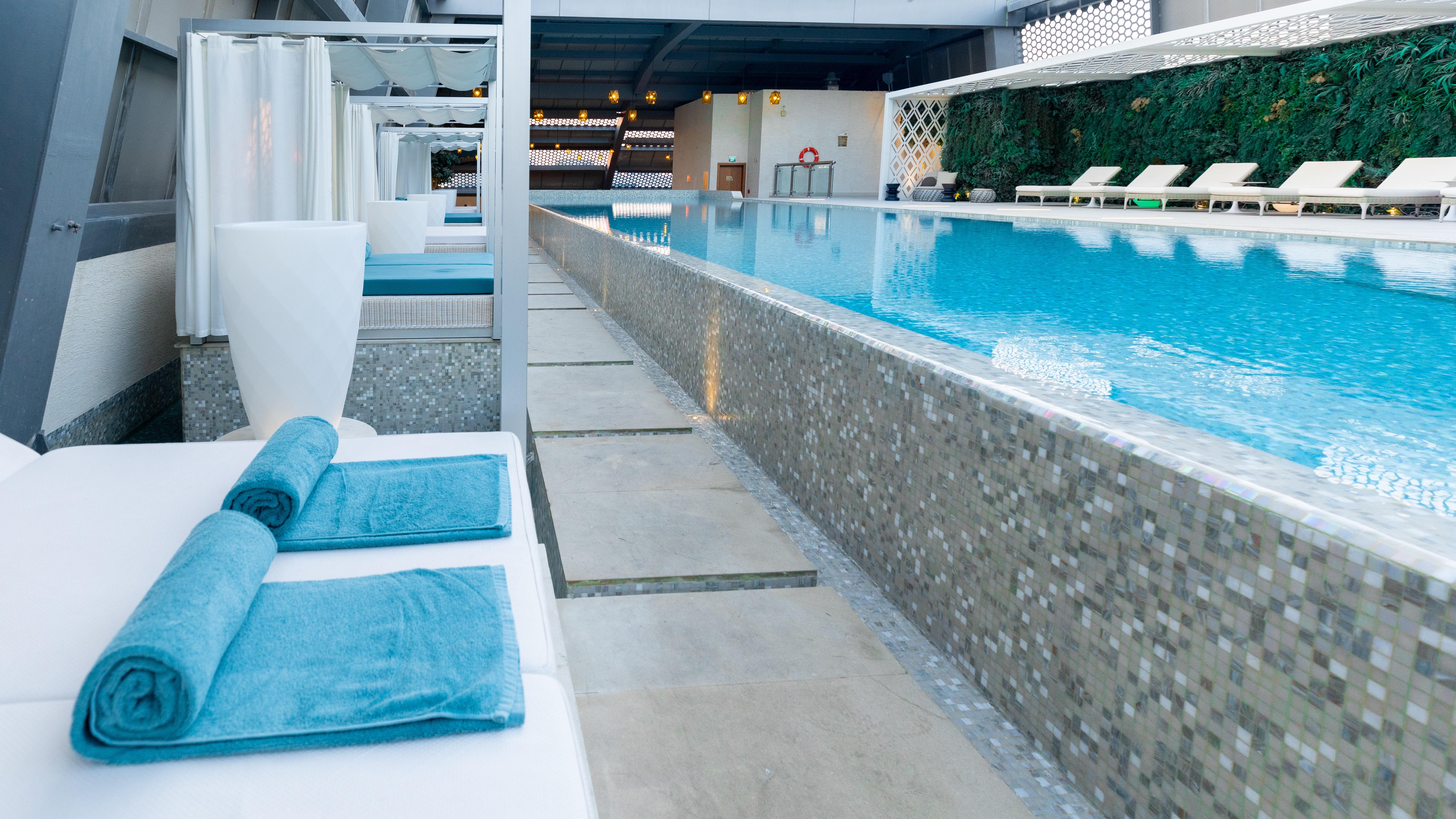 Steigenberger Hotel Doha Exterior foto The photo shows a serene swimming pool area featuring a long, rectangular pool with clear blue water. Surrounding the pool are minimalist white lounge chairs and cabanas, creating a relaxing atmosphere. The pool is bordered by a stone or tile pathway