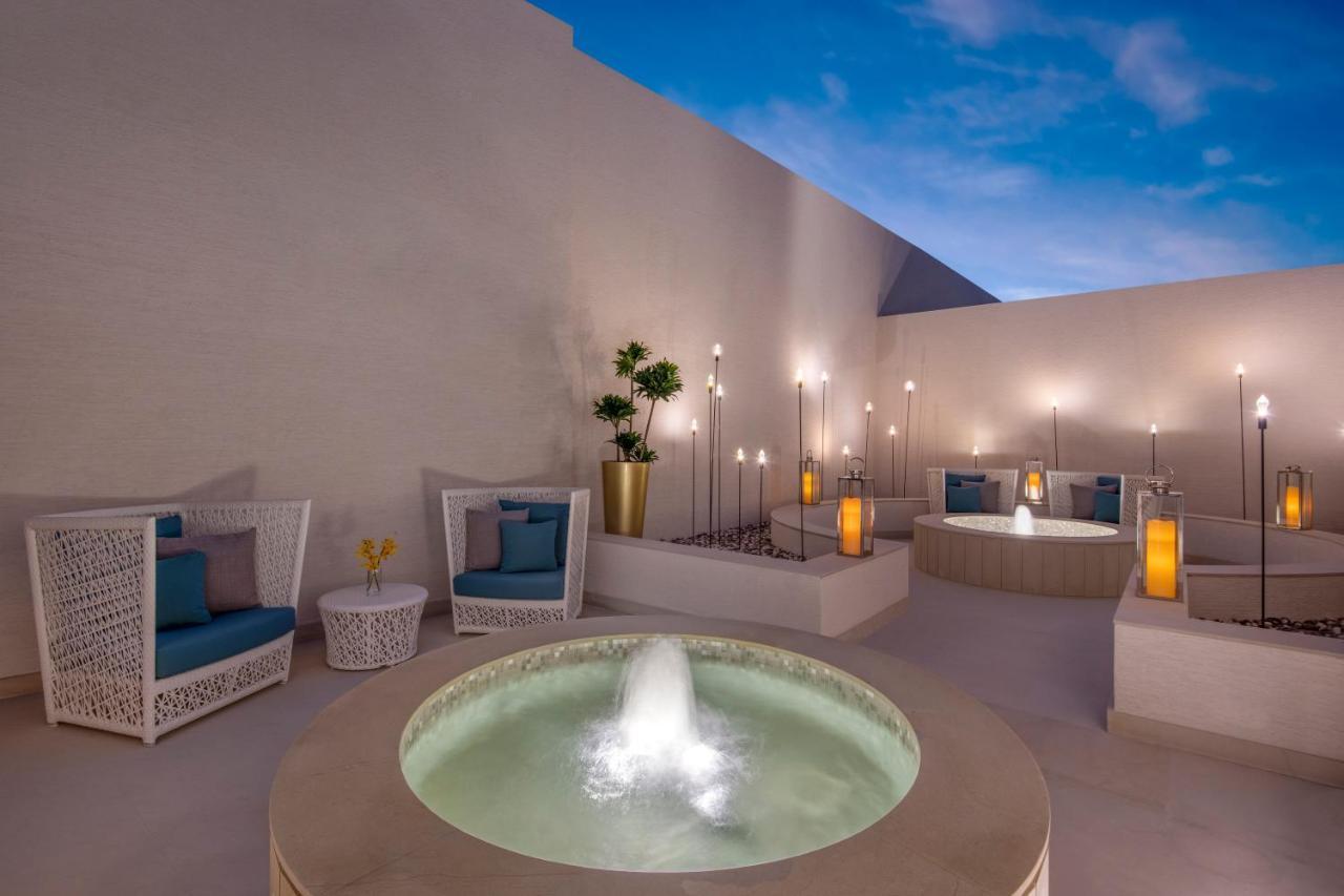 Steigenberger Hotel Doha Exterior foto The photo depicts a serene outdoor space featuring a modern and stylish design. Central to the image is a round stone fountain with water gently flowing from it, creating a tranquil atmosphere. Surrounding the fountain are comfortable seating areas w