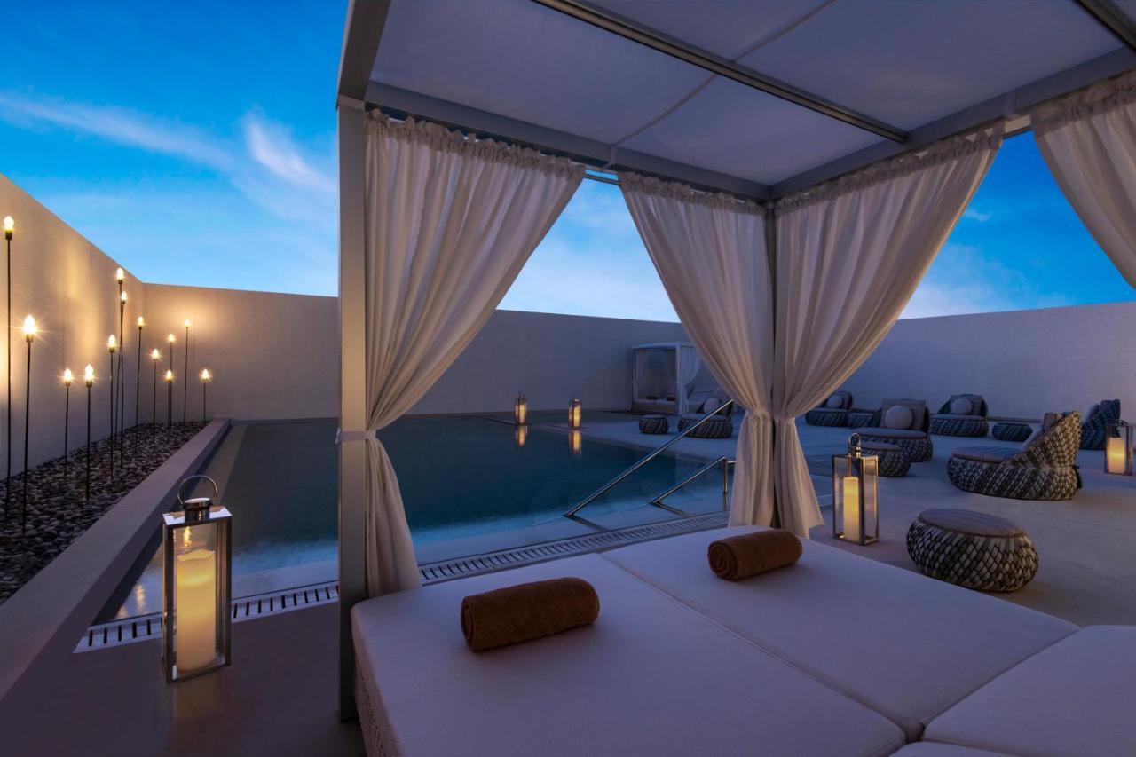 Steigenberger Hotel Doha Exterior foto The photo shows a serene outdoor setting, likely at a luxury resort or spa. In the foreground, there is a structure resembling a cabana with sheer white curtains that create a private space. Inside, there are comfortable beds with rolled towels. 

In