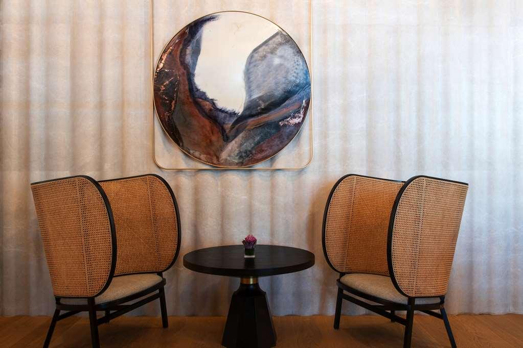 Steigenberger Hotel Doha Restaurante foto The photo showcases a stylish and modern seating area featuring two elegantly designed chairs with curved, woven backs and light-colored cushions. Between the chairs is a small round table with a black base. Above the table hangs a large circular art